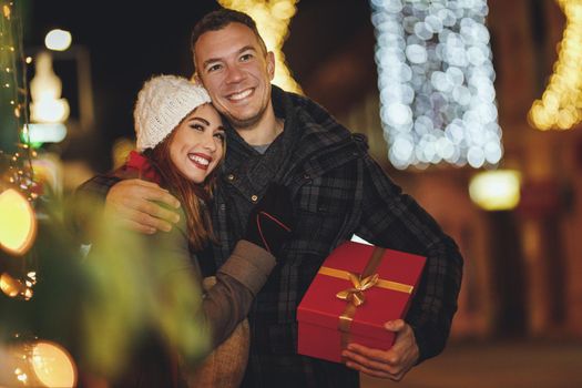 Shoot of a lovely young couple are having fun in the city street at the Christmas night. They are laughing and buying presents for holidays to come.