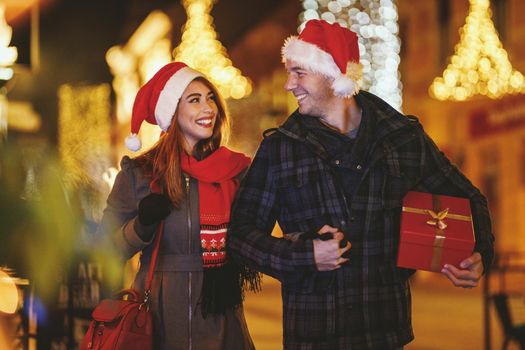 Shoot of a cheerful young couple are having fun in the city street at the Christmas night. They are walking and buying presents for holidays to come.