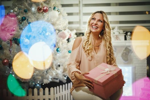 Shot of an attractive young woman opening her Christmas gift by a white Christmas tree at the home.