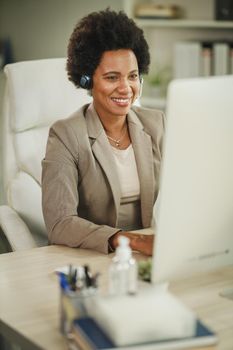 Shot of an African businesswoman wearing a headset while working on her computer during COVID-19 pandemic.