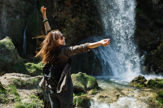 A cheerful young woman enjoying the view of the beautiful waterfall.