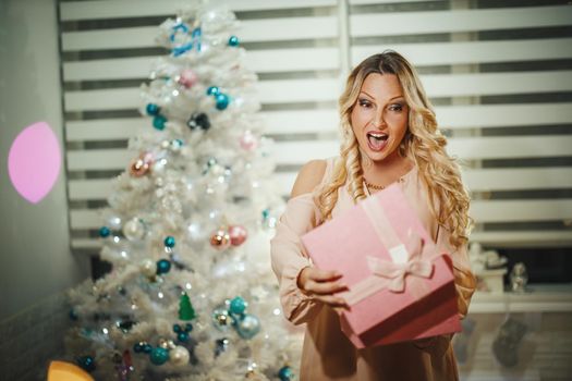 Shot of an attractive young woman opening her Christmas gift by a white Christmas tree at the home.