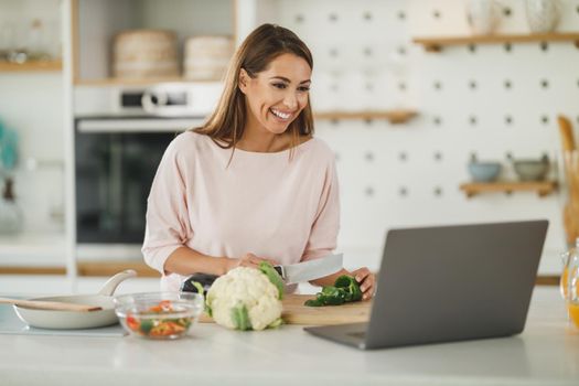 Shot of a young woman using a laptop while preparing a healthy meal at home.