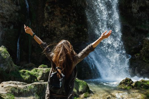 Rear view of a happy young woman enjoying the view of the beautiful waterfall.