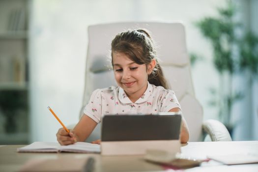 A cute little girl using her digital tablet to do a online lesson at home.