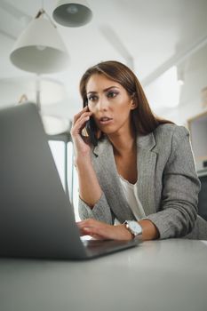 Shot of a multi-tasking young business woman talking on her smartphone and using laptop in the office.