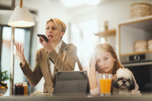 Shot of a frustrated teenage girl sitting with her cute dog waiting for her stressed mom to finish talking on smart phone at her home while getting ready to go to work.