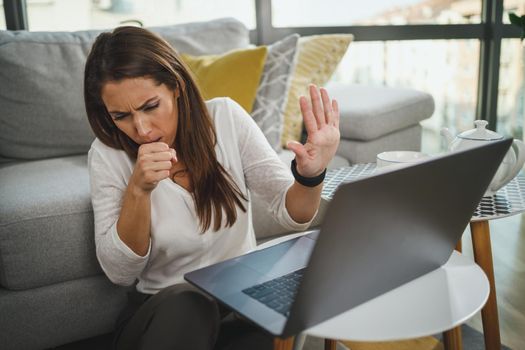 Shot of an beautiful young woman sitting on carpet in her living room and making video call on laptop at her home during corona virus pandemic.