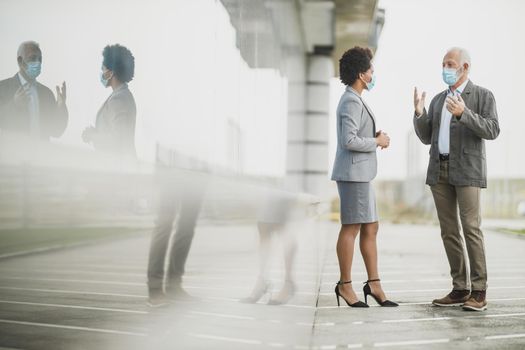 Shot of two successful multi-ethnic business people with protective mask having a discussion in front of the office building during COVID-19 pandemic.