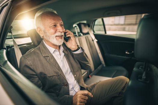 Shot of a successful senior businessman talking on a smartphone while sitting in the backseat of a car during his morning commute.