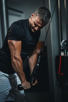 Shot of a muscular guy in sportswear working out at the gym. He is doing cable triceps pulldowns during a strength training.