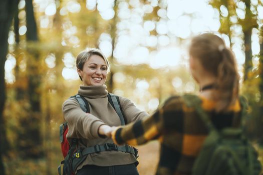 Shot of a teen girl and her mom having fund during walk together through the forest in autumn.