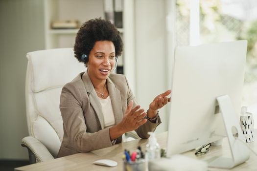 Shot of an African businesswoman with headphones having video call while working on computer during COVID-19 pandemic.