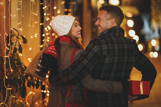 Shoot of a cheerful young couple are having fun in the city street at the Christmas night. They are laughing and buying presents for holidays to come.