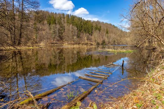 A spring day around burgk castle in the saaletal. Reflection of the sky, clouds, forest in the Saale river. In the foreground is a wooden staircase in the river. Germany, Thuringia. 