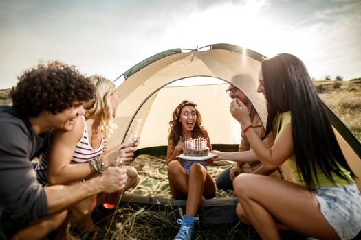 A group of cheerful friends having fun and celebrating a birthday outside their tent at a festival.