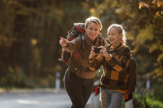 Shot of a teen girl and her mom using digital photo camera during walk together through the forest in autumn.