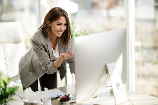 An attractive young woman using a computer to have a web conference in her home office.