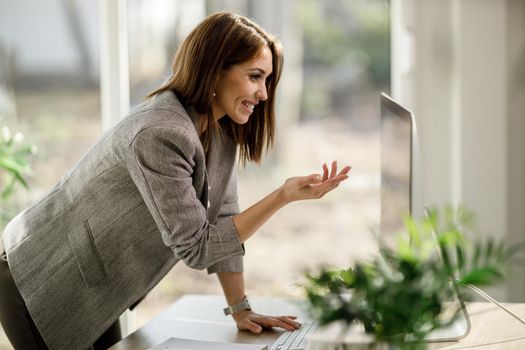 A smiling young woman using a computer to have a web conference at home office.
