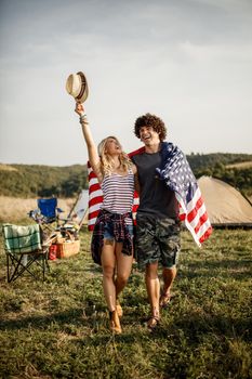 An attractive cheerful couple with american flag partying at the campsite at an outdoor festival.