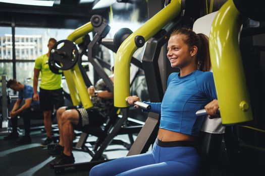 Shot of a muscular young woman in sportswear working out on a cross training at the gym. She is doing exercise for her chest on a machine.
