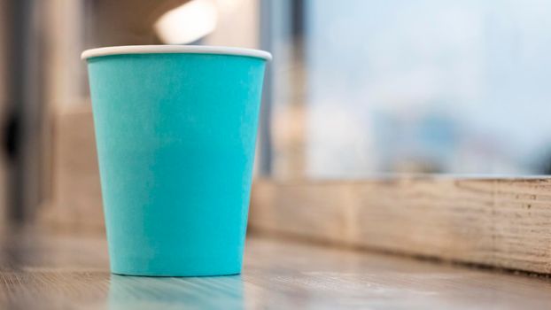 Blue paper cup with coffee on a wooden table, copy space