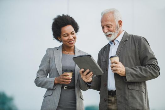 Shot of two successful multi-ethnic business people talking and using digital tablet while having a coffee break outdoors.