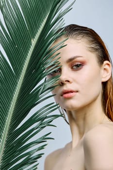 a close beauty portrait of a beautiful woman standing holding a tropical palm leaf in her hand, bringing it to her face. Vertical photo without retouching. High quality photo