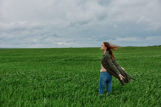 a woman in a long coat stands in tall green grass in a field, in cloudy weather, enjoying nature and the view. High quality photo