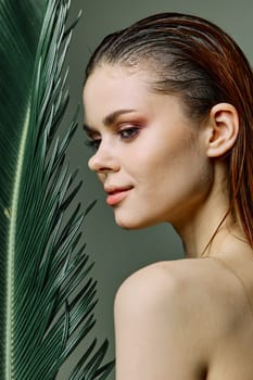 vertical photo, portrait of an elegant woman with slicked back hair, standing with a palm leaf holding it near her face. Photo without retouching. High quality photo