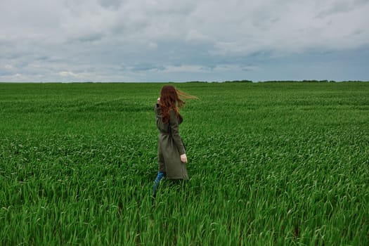 a woman in a long raincoat stands with her back to the camera, far away in a field in rainy, cloudy weather. High quality photo