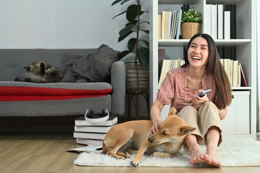 Happy young pretty woman in casual clothes spending time with lovely dog in bright living room.