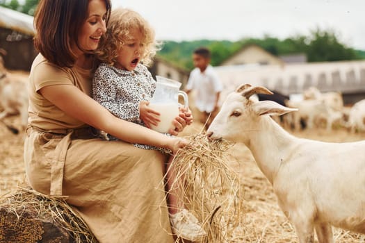 Fresh natural milk. Young mother with her daughter is on the farm at summertime with goats.