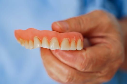 Asian senior woman patient holding teeth denture in her hand for chew food.