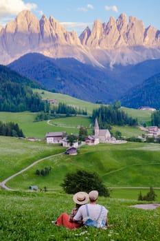 Couple at St. Magdalena Geisler or Odle Dolomites mountain peaks. Val di Funes valley in Italy, Santa Magdalena village Dolomites mountains, men and women on vacation in Italian mountain Alps