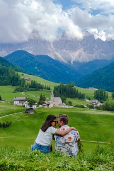 Couple at St. Magdalena Geisler or Odle Dolomites mountain peaks. Val di Funes valley in Italy, Santa Magdalena village Dolomites mountains, men and women on vacation in Italian mountain Alps