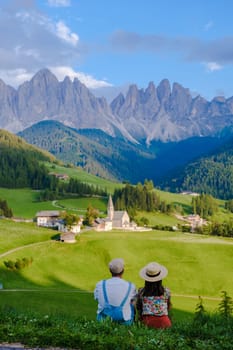 Couple at St. Magdalena Geisler or Odle Dolomites mountain peaks. Val di Funes valley in Italy, Santa Magdalena village Dolomites mountains, men and women on vacation in Italian mountain Alps