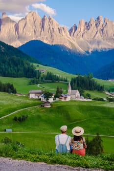 Couple at St. Magdalena Geisler or Odle Dolomites mountain peaks. Val di Funes valley in Italy, Santa Magdalena village Dolomites mountains, men and women on vacation in Italian mountain Alps