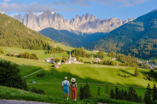 Couple at St. Magdalena Geisler or Odle Dolomites mountain peaks. Val di Funes valley in Italy, Santa Magdalena village Dolomites mountains, men and women on vacation in Italian mountain Alps