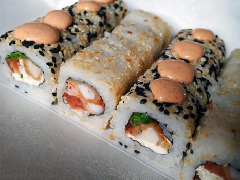 Sushi rolls with fish and cheese, sesame seeds and sauce close-up on the table.