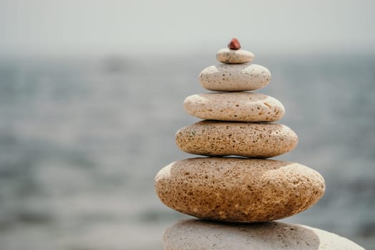 Pyramid stones on the seashore with warm sunset on the sea background. Happy holidays. Pebble beach, calm sea, travel destination. Concept of happy vacation on the sea, meditation, spa, calmness.