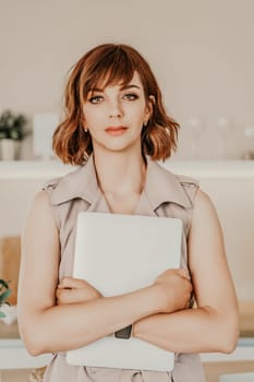 Brunette macbook. Portrait of a woman, she holds a mabuk in her hands and looks at the camera, wearing a beige dress on a beige background