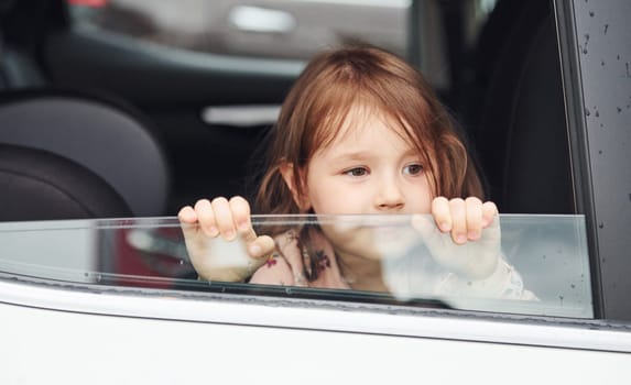 Cute little girl looks through window car. Conception of traveling and vaccation.