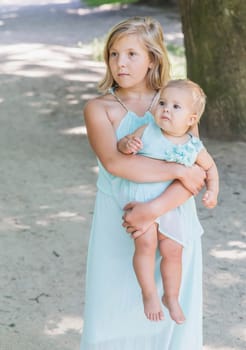 Two sisters in similar blue dresses are walking in the park.