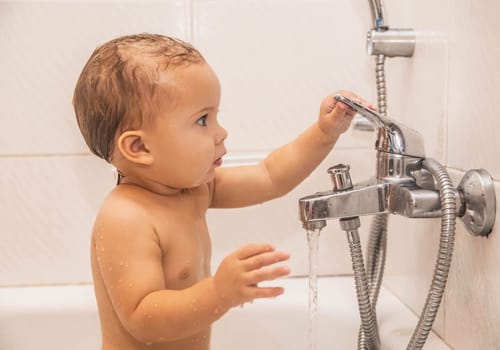 Baby bathes in the bathroom holding on to the water tap.