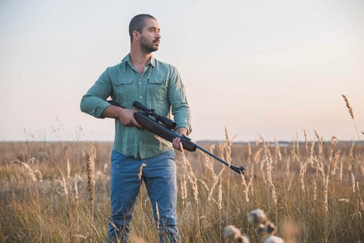 man with a rifle with a telescopic sight stands in a field.