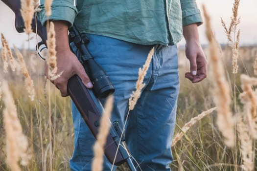 man with a rifle with a telescopic sight stands in a field.