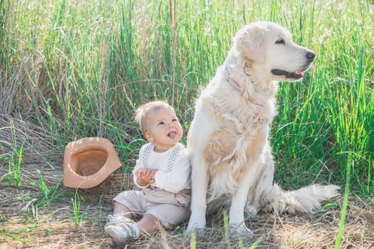 blond baby in a suit with suspenders sticks tongue out to dog.