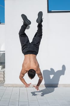 Man doing a handstand outdoors against a white wall