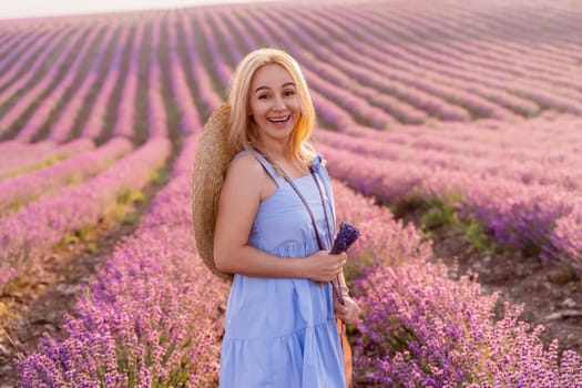 Woman lavender field sunset. Romantic woman walks through the lavender fields. illuminated by sunset sunlight. She is wearing a blue dress with a hat